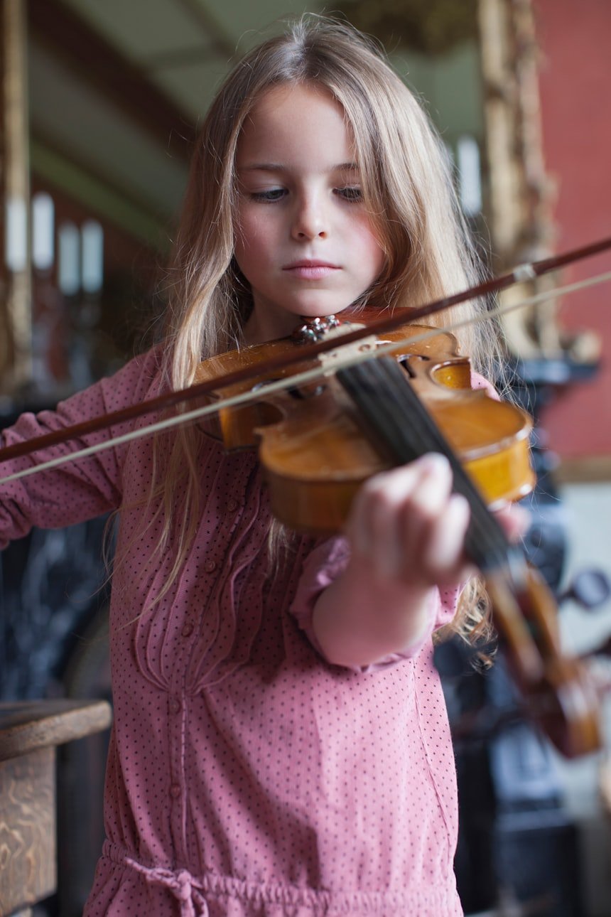Little girl playing violin in a room — young student focused and engaged